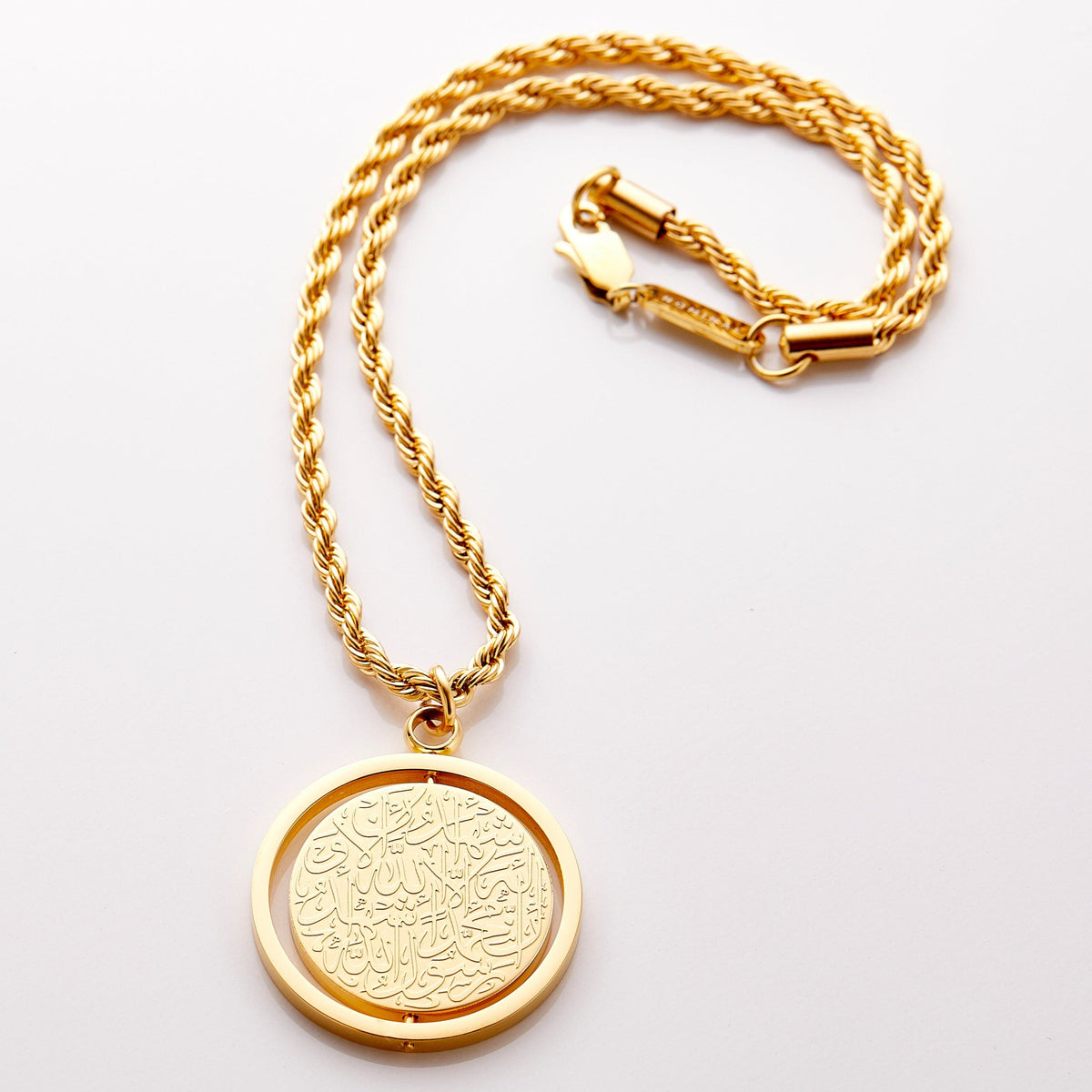 Gold car hanger with a circular pendant engraved in Arabic calligraphy of the Shahada, styled flat against a neutral background.