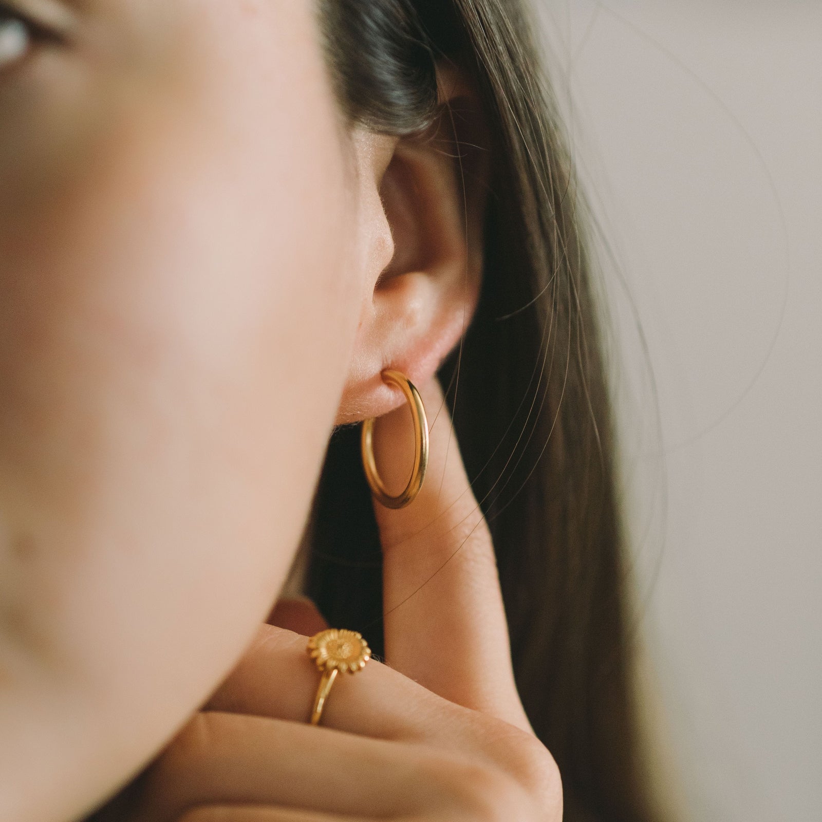 Close-up of a woman wearing gold hoop earrings, hand near the earring with a gold ring on her finger.