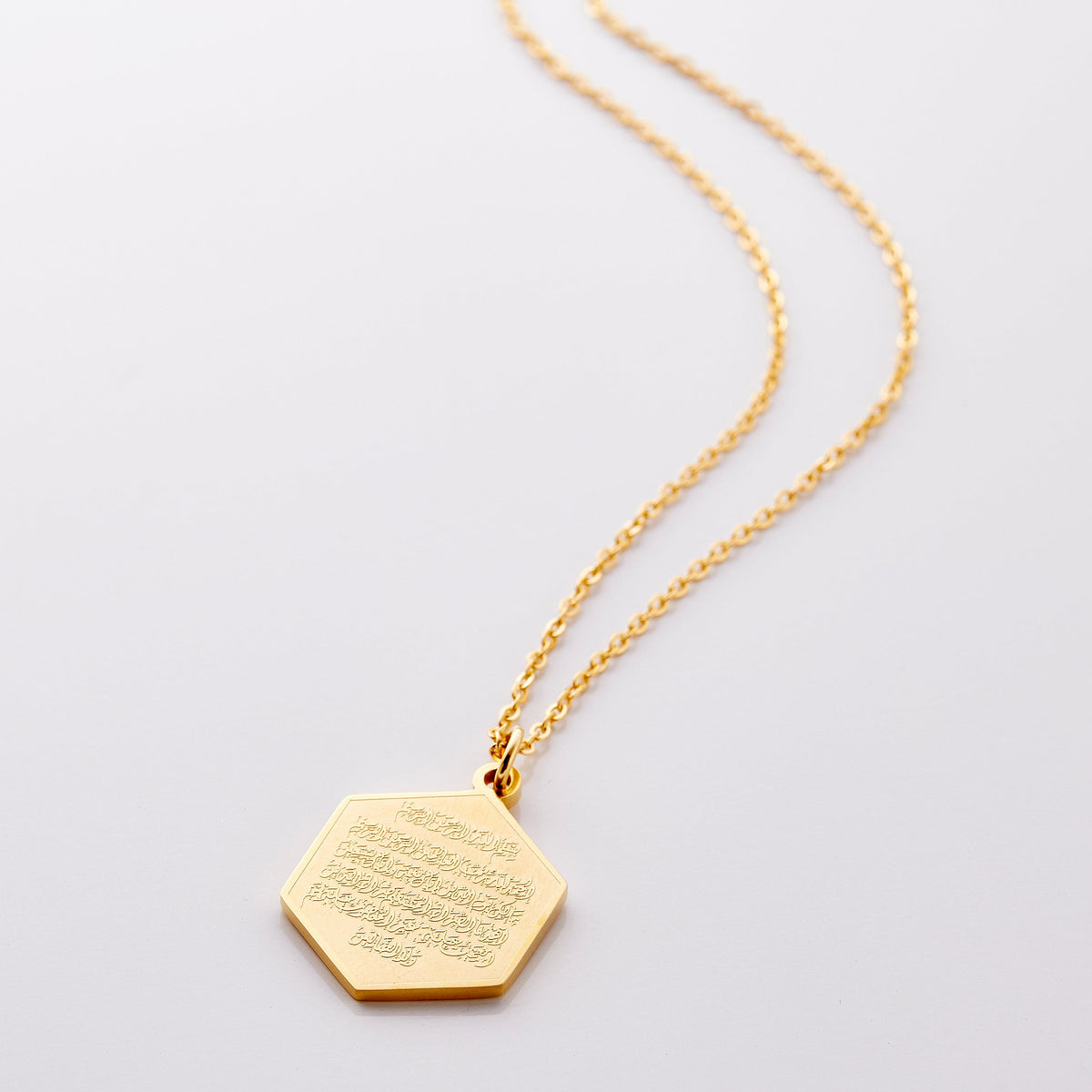 Flat lay of the gold Surat Al-Fatiha Necklace against a light background. This piece is engraved with the entirety of the opening chapter of the Qur'an 