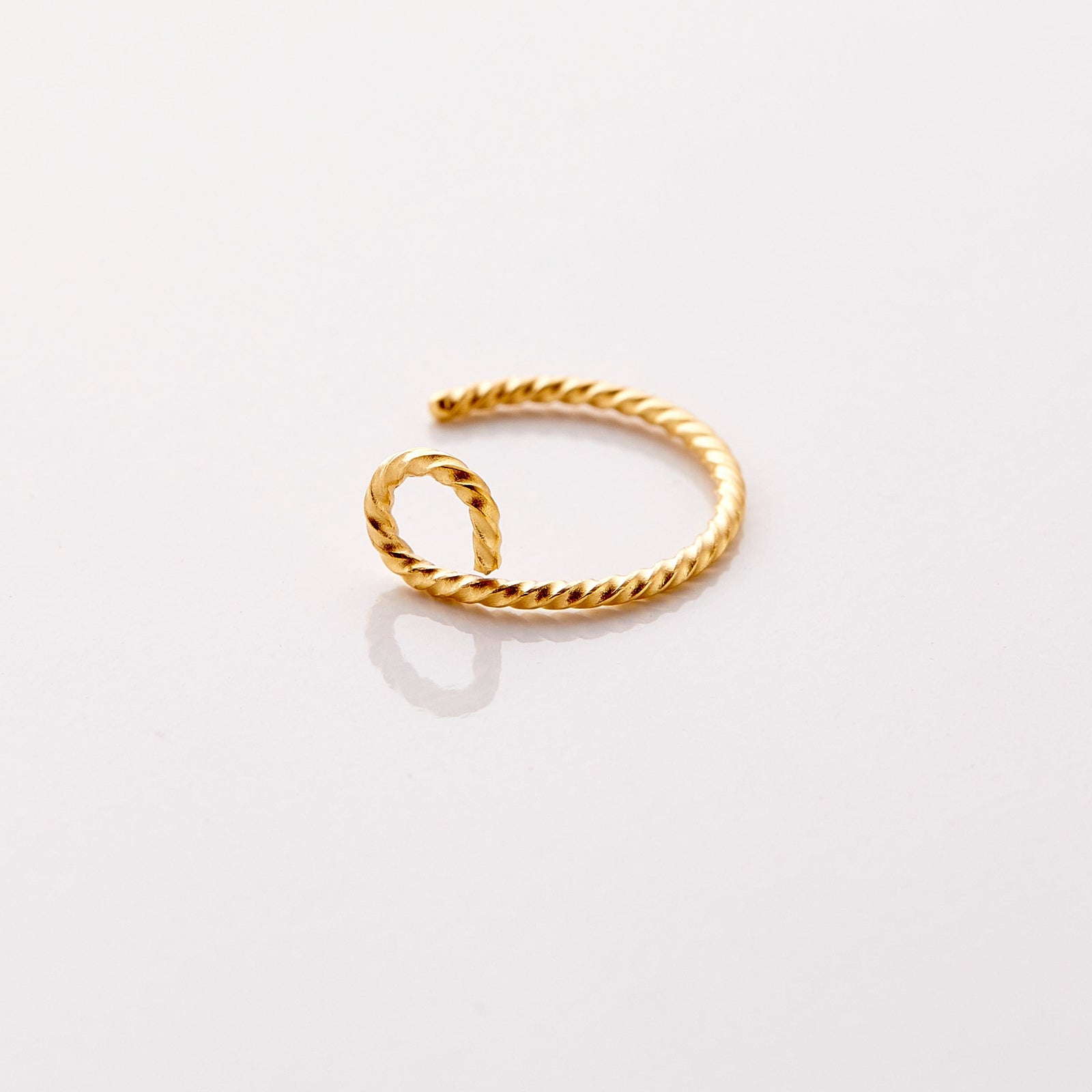 Photo of an 18k gold plated nose hoop marked with a spiraling patter against a light background.