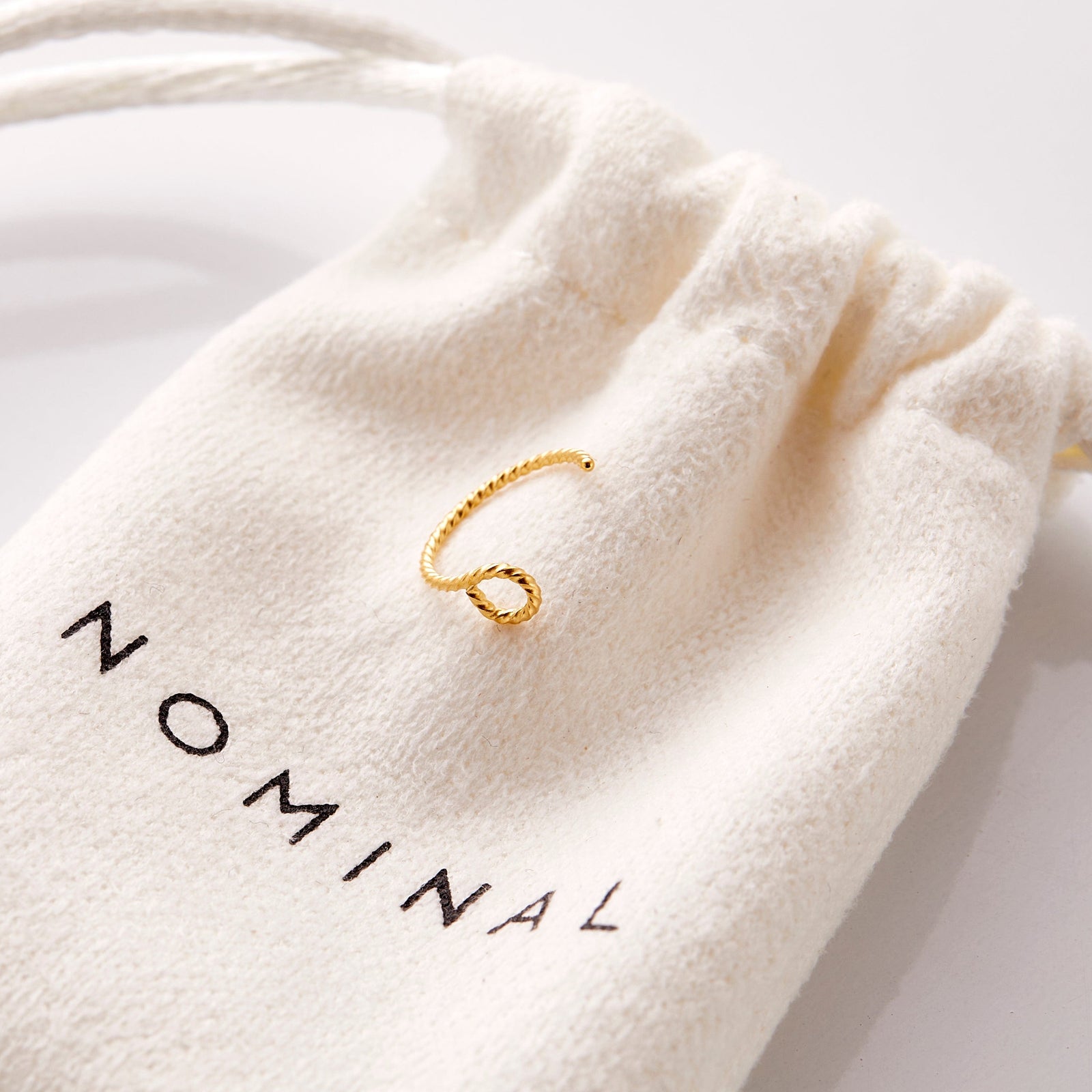 The gold Twirl Nose Hoop resting on the nominal pouch