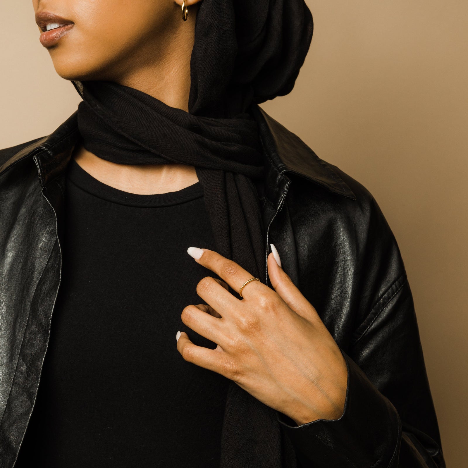Woman in a black scarf and leather jacket wearing the gold twist ring on her hand, holding her scarf.