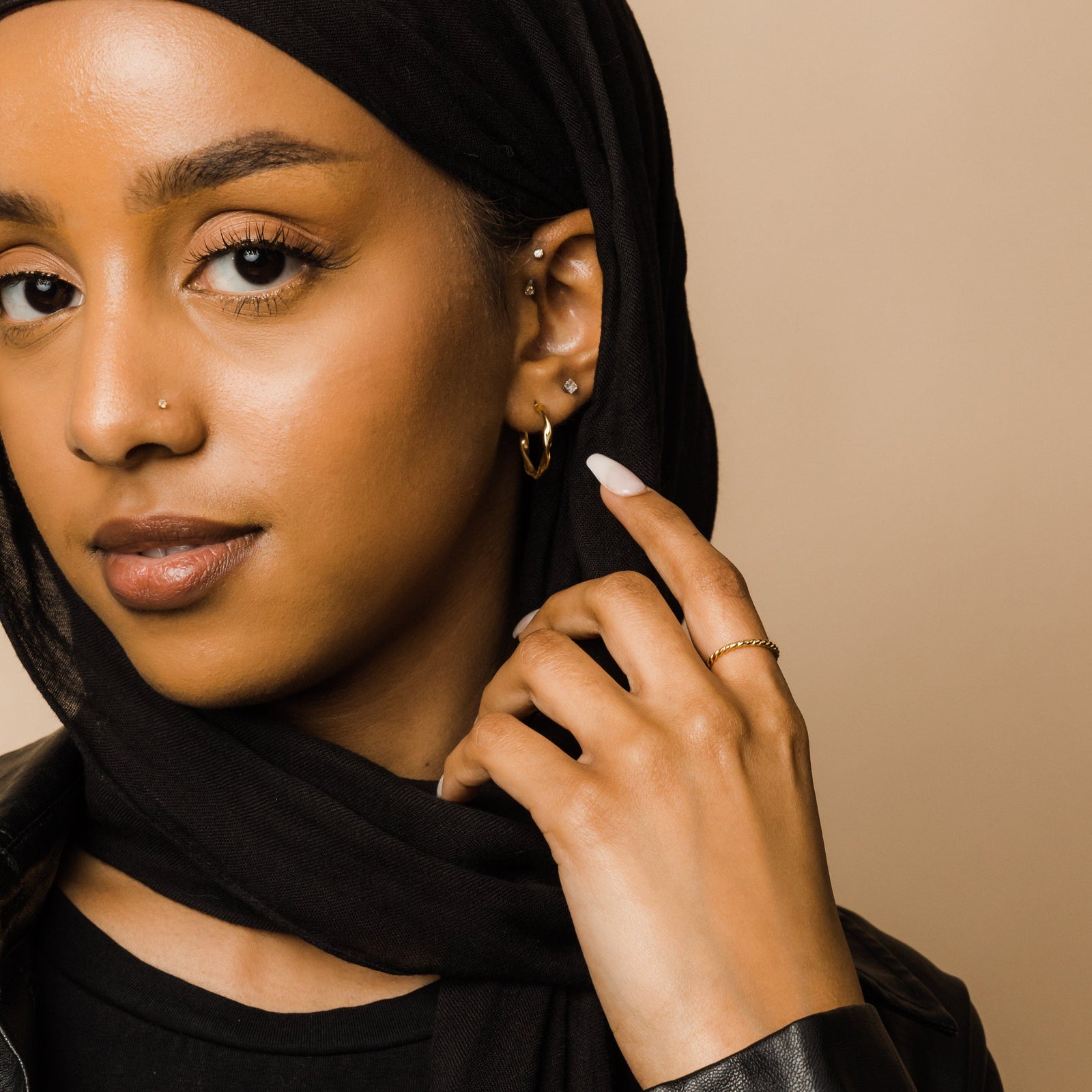 Woman in a black scarf wearing the gold twist ring, hand gently raised to her face.