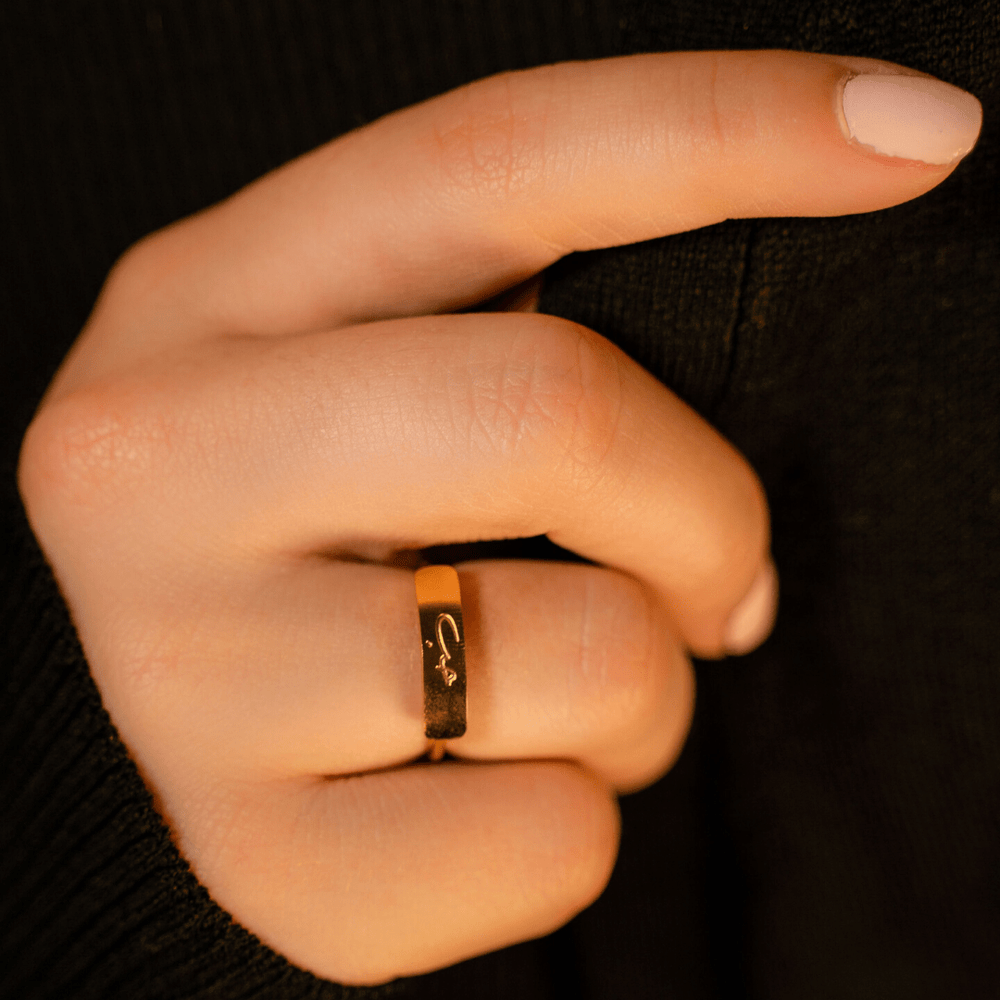 Hand wearing the gold Love Bar Ring with the Arabic word "Love" engraved on the flat bar centerpiece, styled against a dark background.