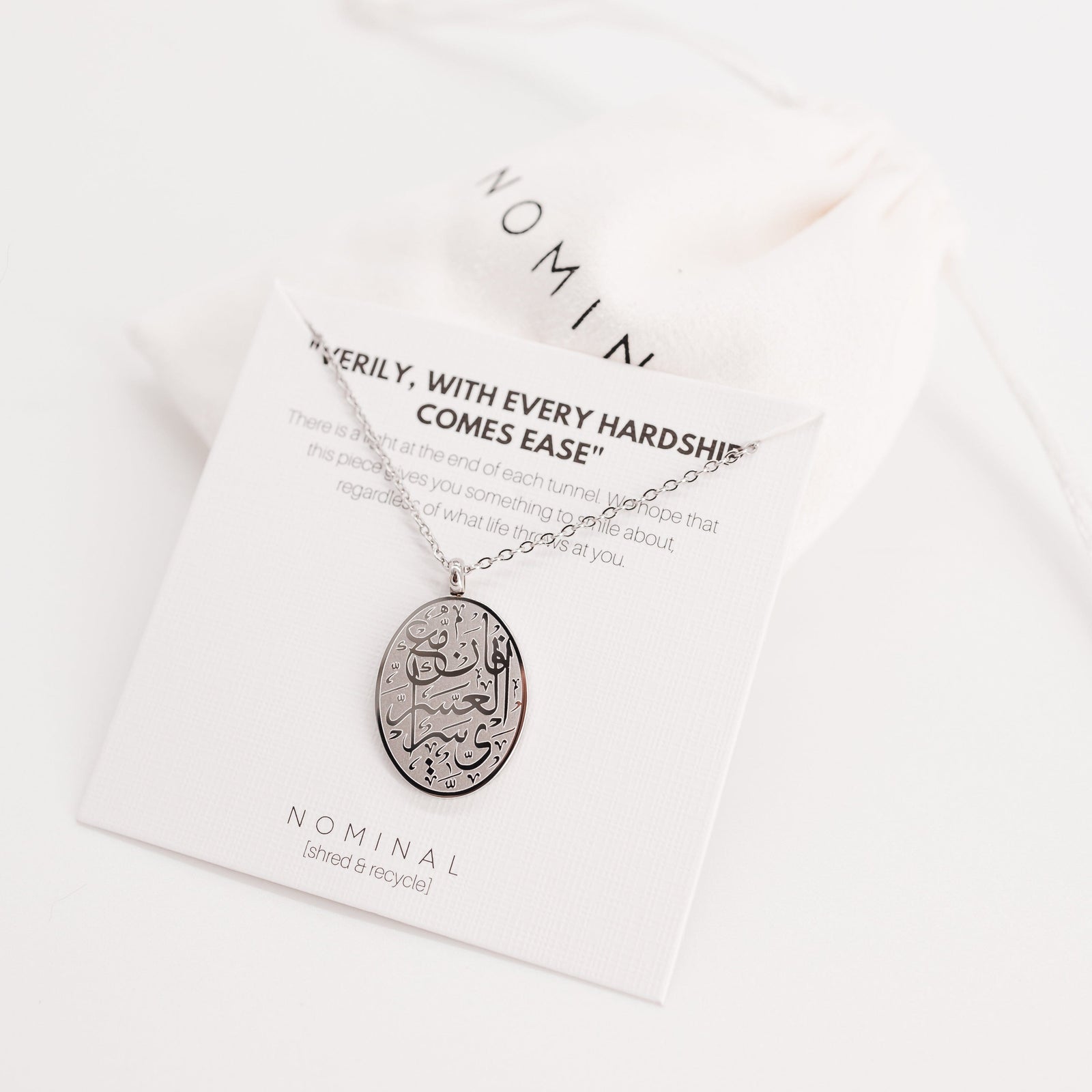 Photo of the silver "Verily, with Hardship Comes Ease" Oval Necklace on its packaging.
