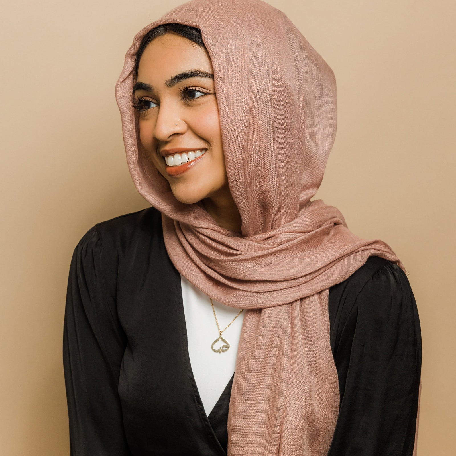 Photo of the model looking away and smiling. The model is wearing the gold Love Heart Calligraphy Necklace