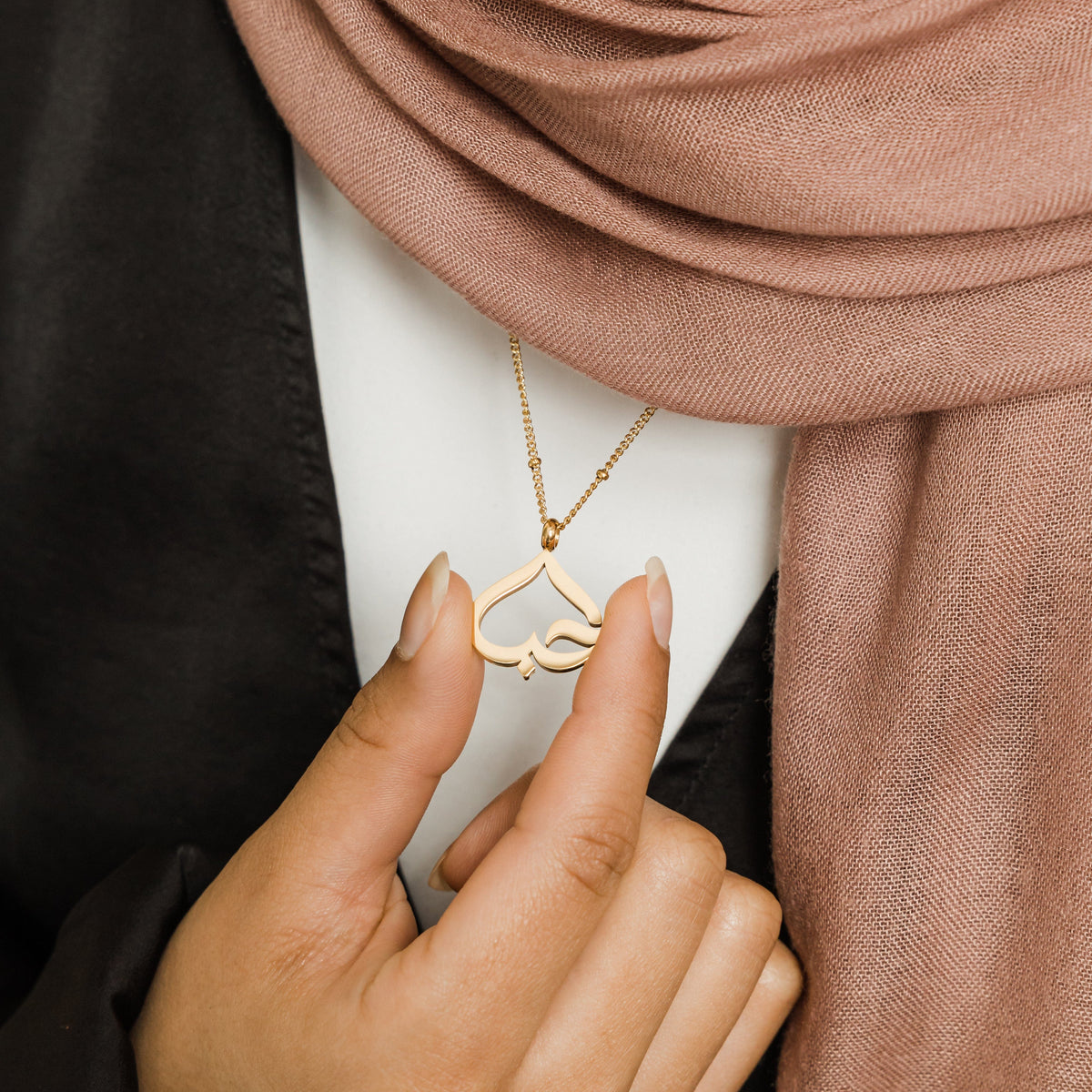 Close up of the gold Love Heart Calligraphy Necklace as worn by the model.