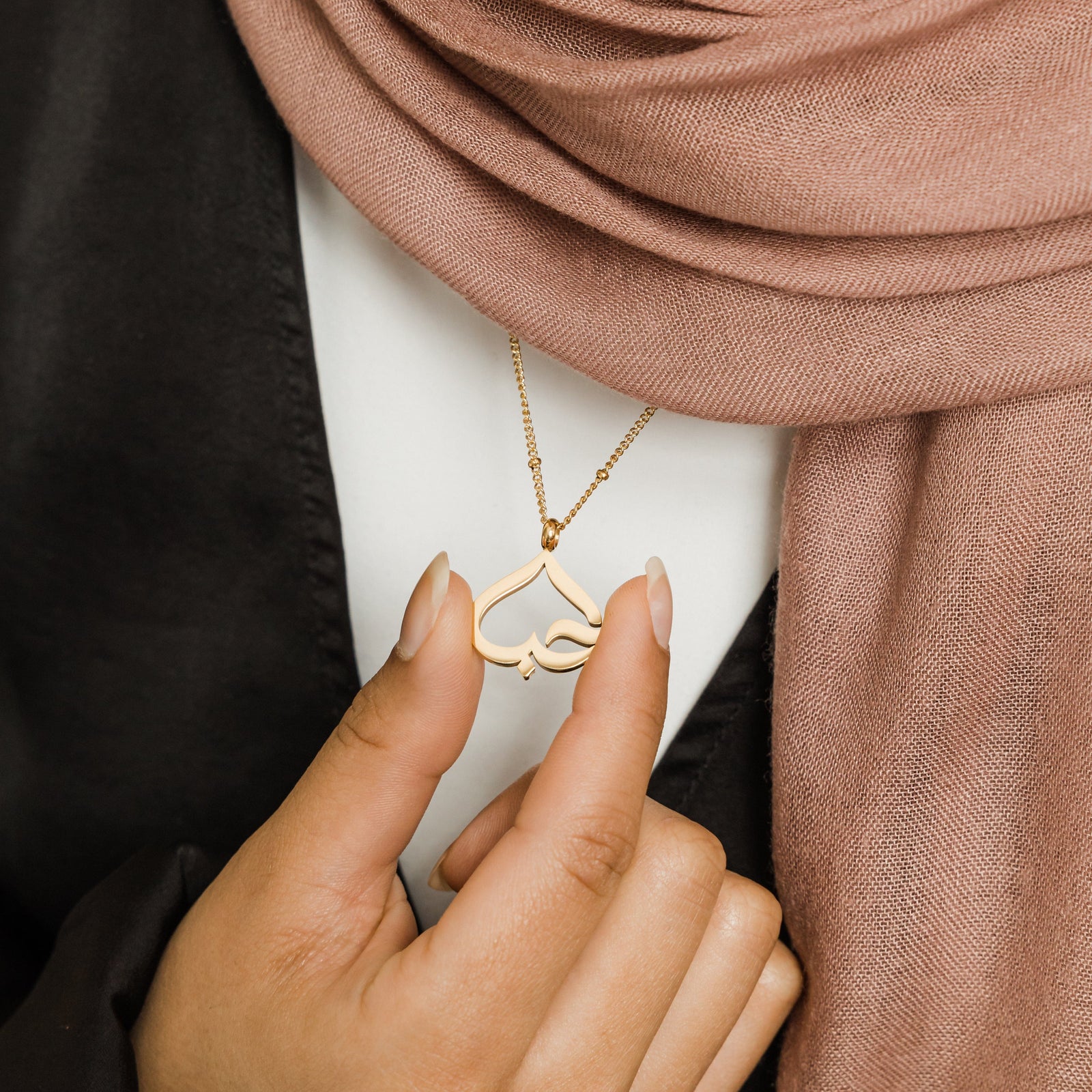 Close up of the gold Love Heart Calligraphy Necklace as worn by the model.