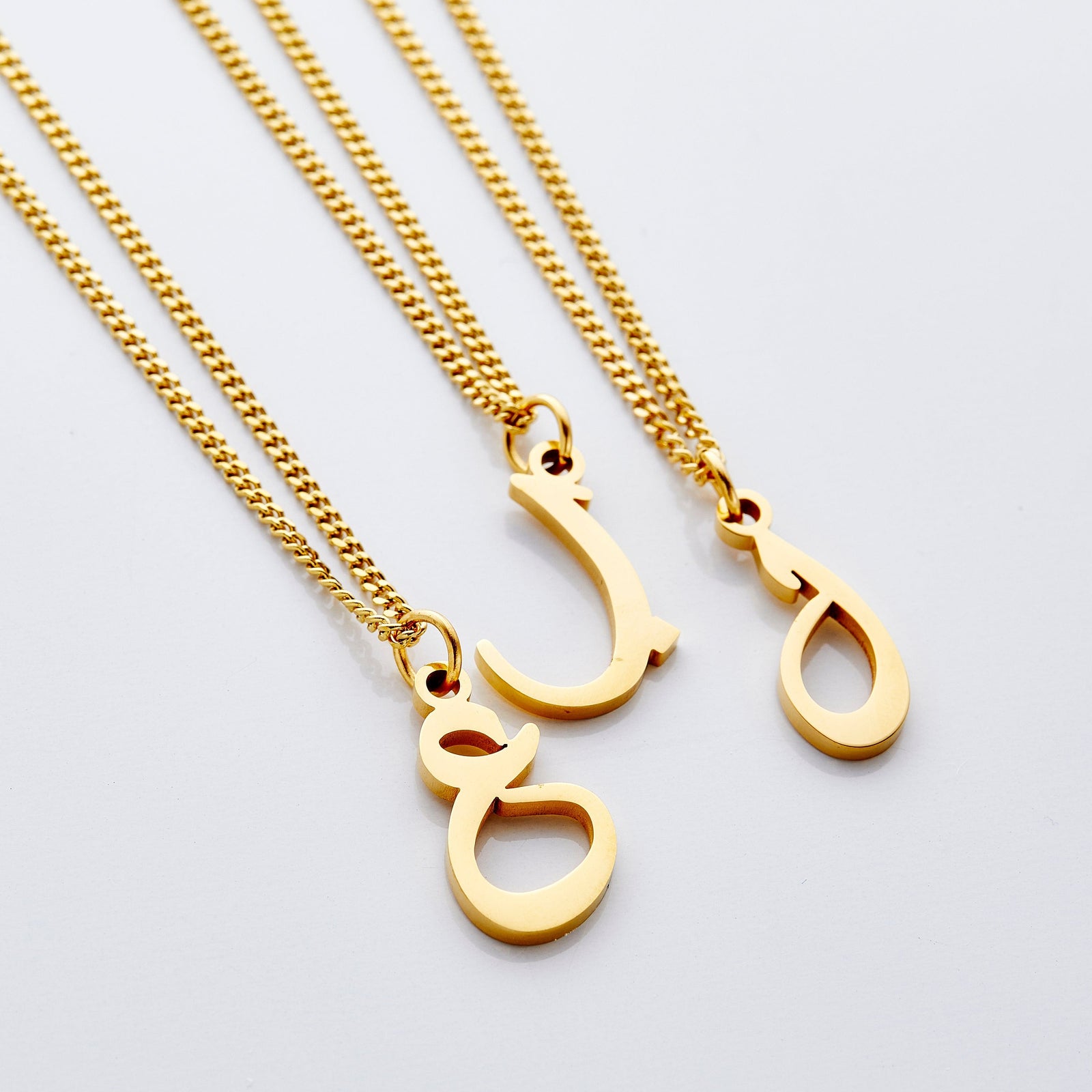 Flat lay of three Hanging Arabic Letter Necklaces  in different letters.