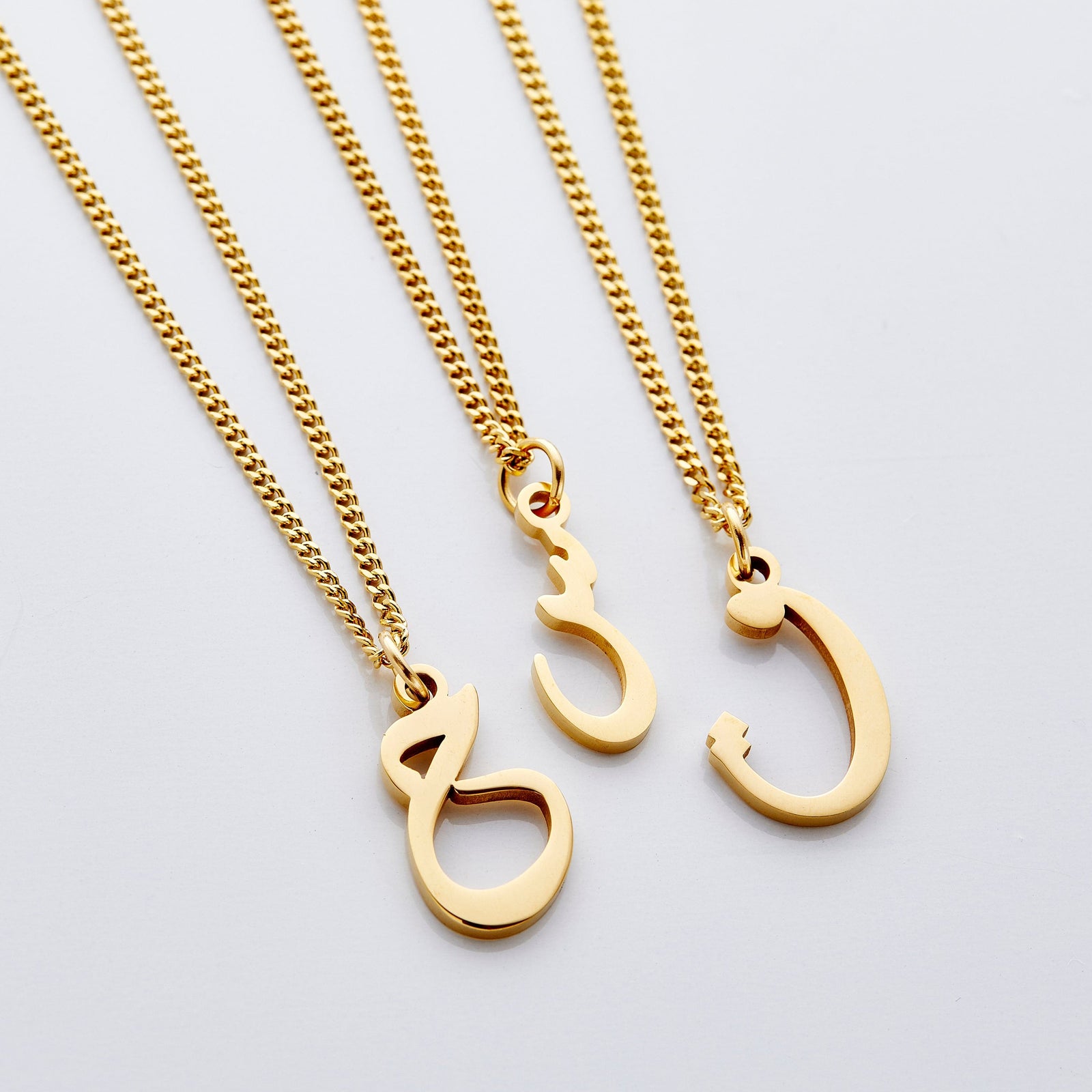Flat lay of three Hanging Arabic Letter Necklaces  in different letters.