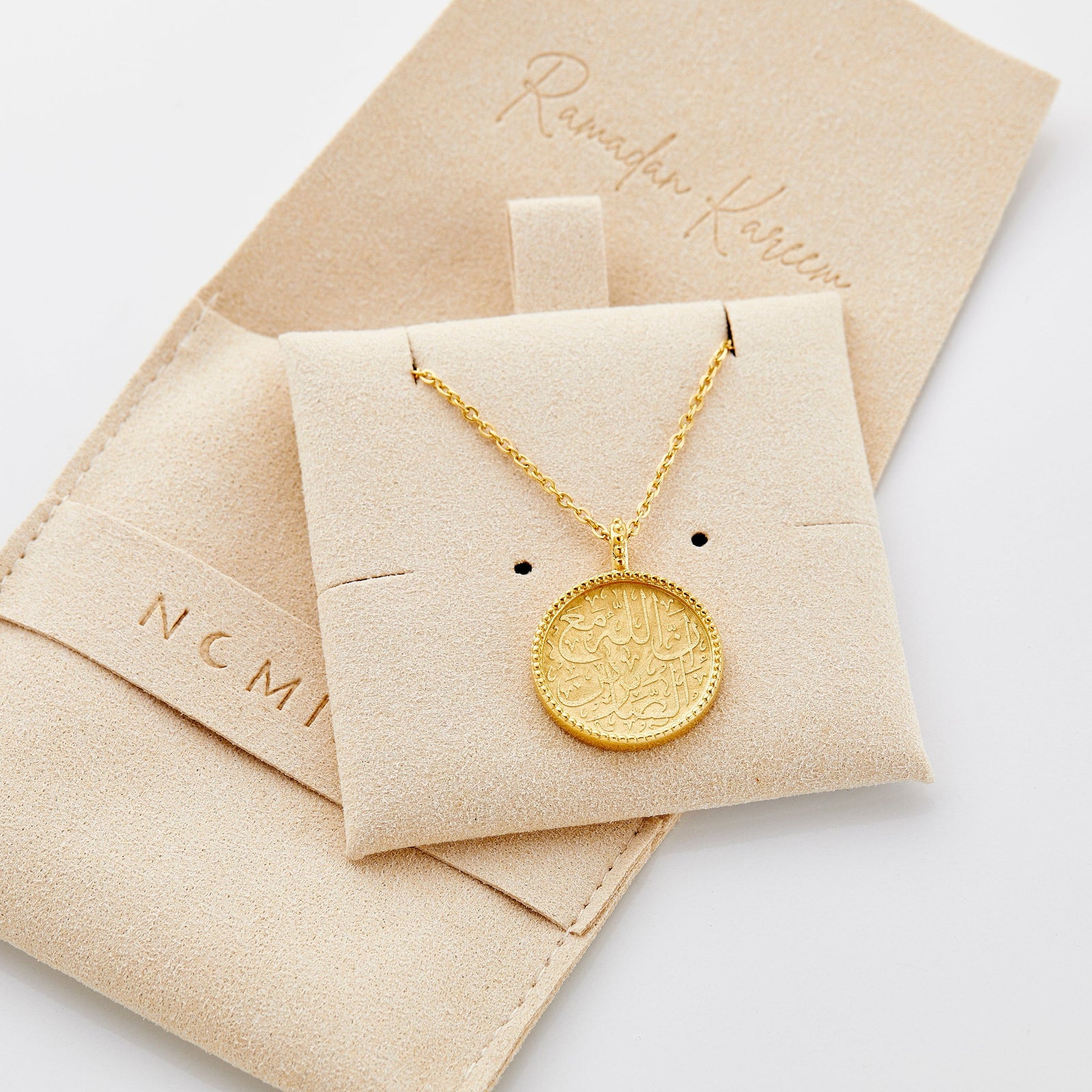 Close up of the gold Patience Token Necklace on its packaging.