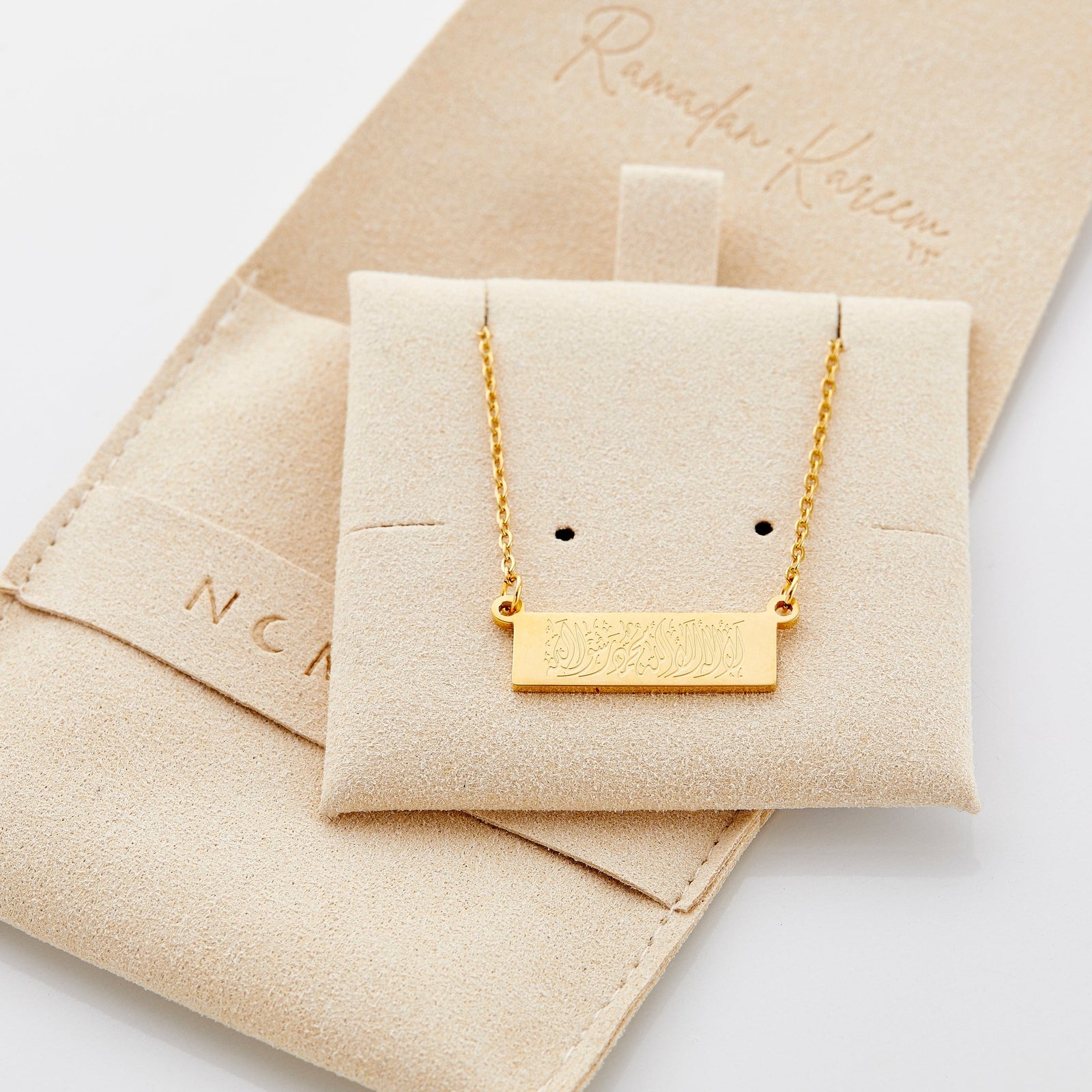 The gold Shahada Bar Necklace displayed on the Nominal packaging.