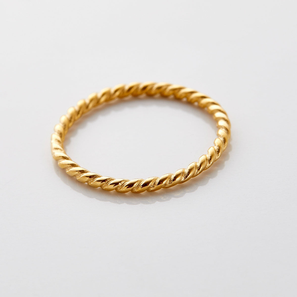 Gold twist ring featuring a delicate rope-like design with a polished finish, displayed flat on a white surface.