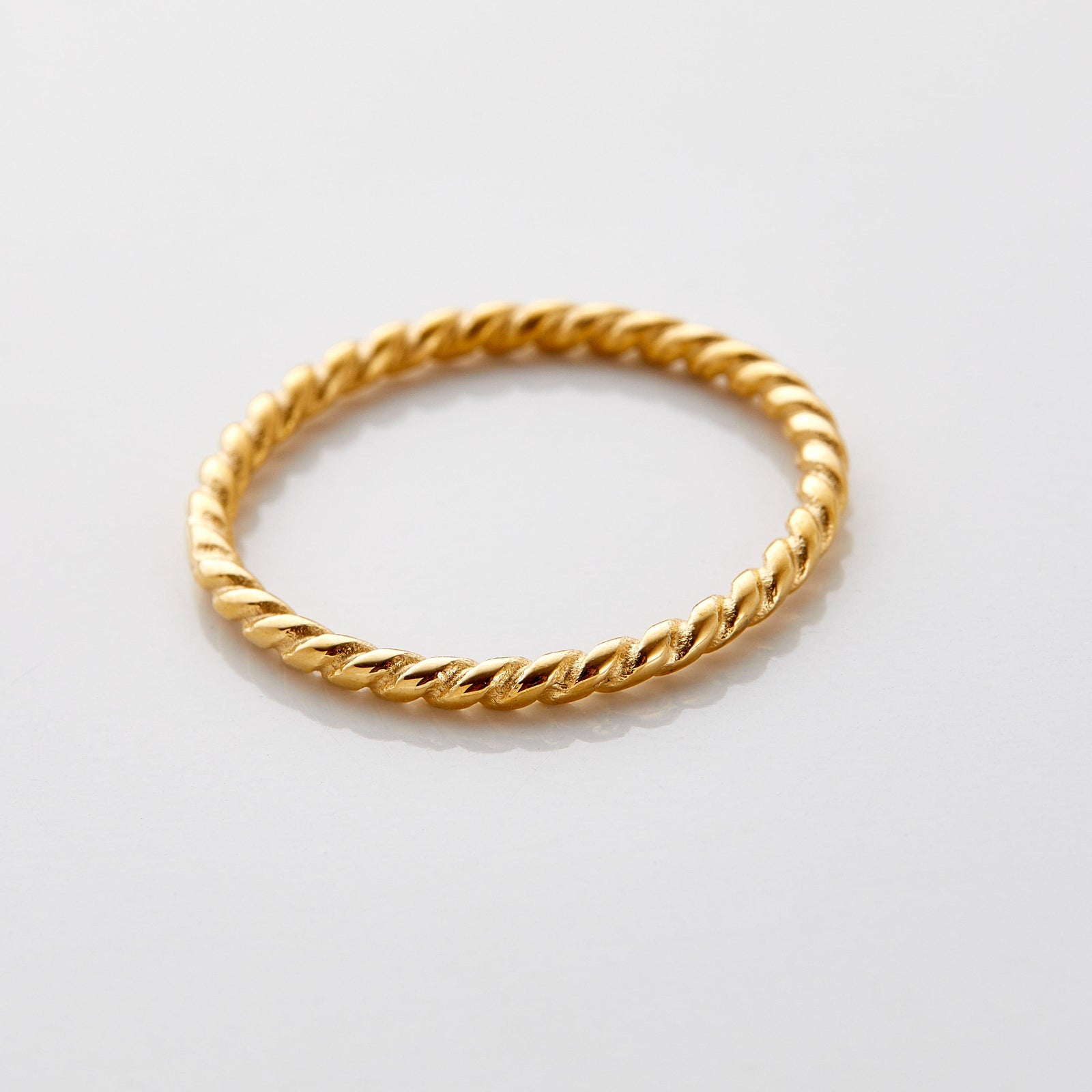 Gold twist ring featuring a delicate rope-like design with a polished finish, displayed flat on a white surface.