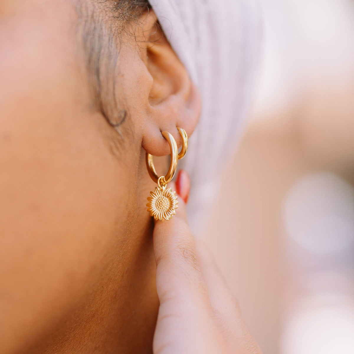 Close up of the Sunflower Mini-Hoop Earrings as worn by the model on their left ear.
