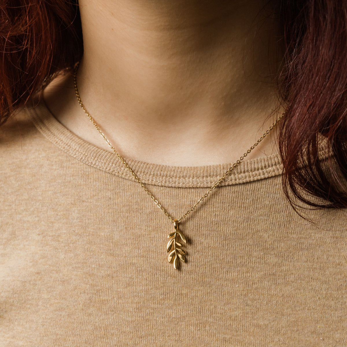 Close up of the gold Palestine Olive Branch Necklace as worn by a model.
