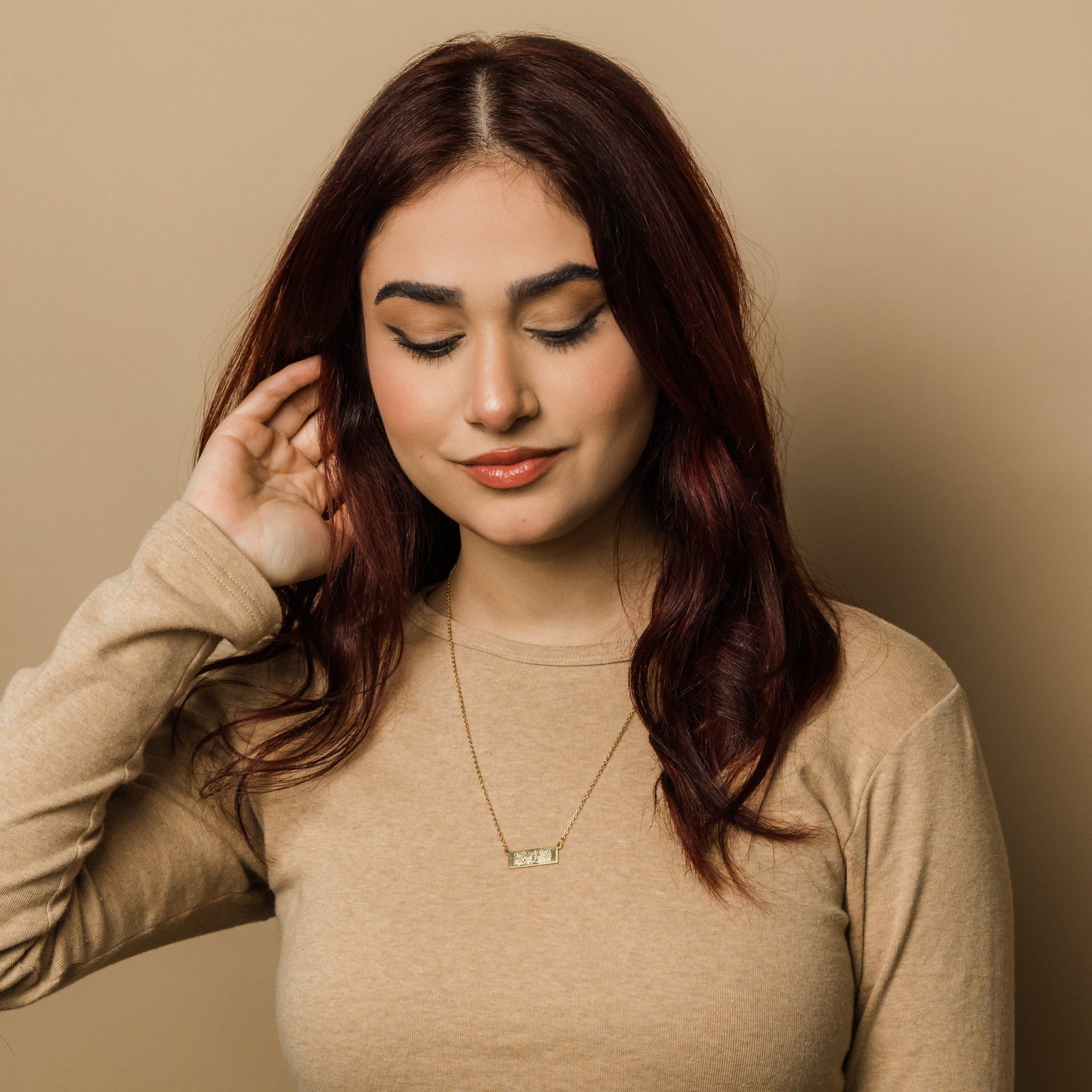 Photo of the model looking down. The model is wearing the gold Shahada Bar Necklace.